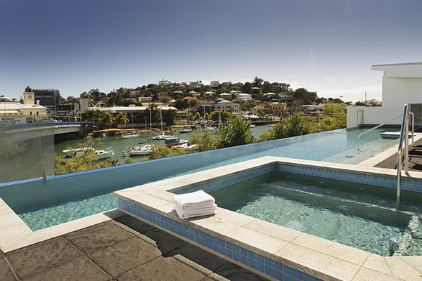 infinity swimming pool with deckchair, towel and spa and view of Ross Creek in Townsville with sun setting
